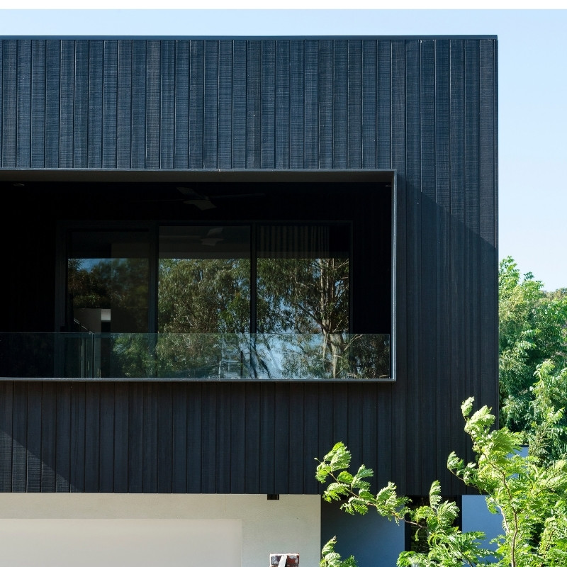 A contemporary building with a white rendered first storey and a black timber clad second storey.