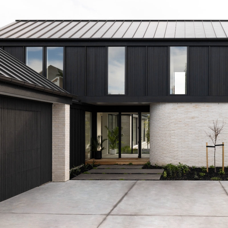 MillworksLtd_Abodo_JonoParker_ClimateConsciousShowcase_GarageDoorCladding Modern home with black timber cladding on first storey and garage doors.