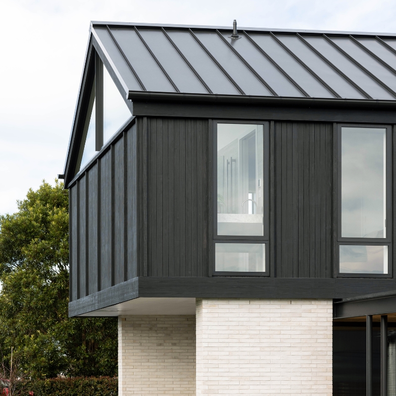 Contemporary home with black timber cladding on top floor, contrasting with white brick plinth.