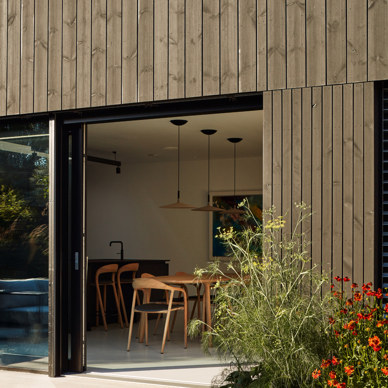 MillworksLtd-ThemoWood-Pine-Black-Cladding Black ThermoWood® Pine exterior cladding surrounding open sliding door with view into modern kitchen.