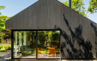 A modern house with a minimalist design. The exterior is finished in Millworks vertical Charcoal Black Thermowood timber cladding. The surrounding greenery contrast with the dark wood, creating a harmonious balance between the building and nature.